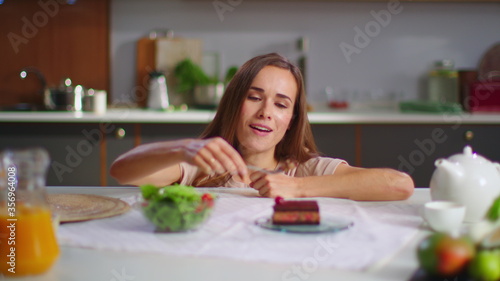 Happy woman eating cake instead salad on kitchen. Lady enjoying cake at table © stockbusters