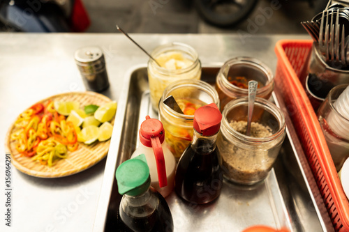 Traditional Vietnamese noodle condiment tray with dish of lemon slices, jar of chili, fish sauce, soy sauce, spoons and chopsticks at street food cart in Ho Chi Minh city, Vietnam