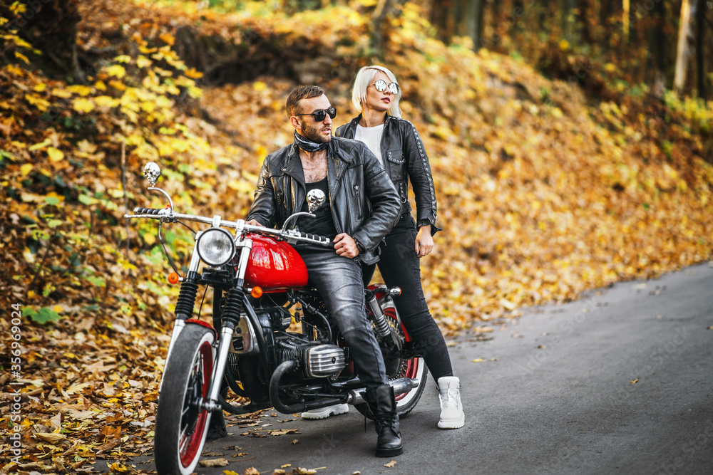 Obraz premium Pretty couple near red motorcycle on the road in the forest with colorful blured background