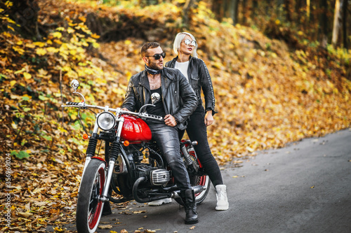Fototapeta Naklejka Na Ścianę i Meble -  Pretty couple near red motorcycle on the road in the forest with colorful blured background