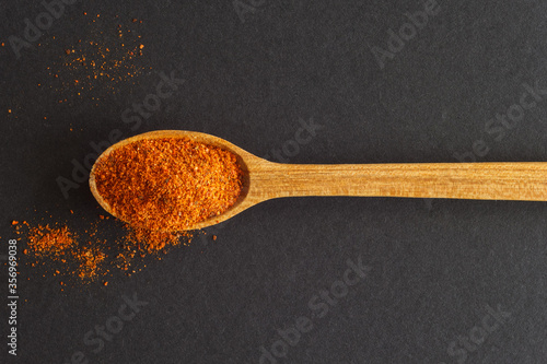 A wooden spoon with hot milled pepper on a dark background. View from the top