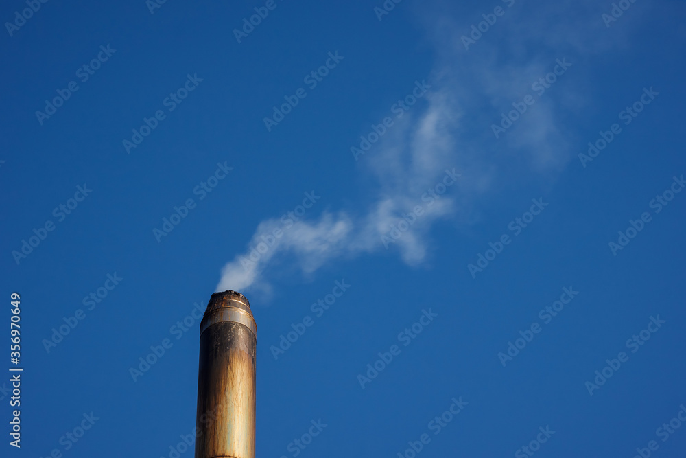 Metal smoke pipe with smoke on blue sky background. Copy space. Metal smoke pipe with smoke on blue sky background. Copy space.