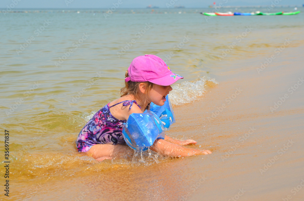 A happy child is swimming in the sea. Little girl on the beach in summer lifestyle. A fun pastime and active sportive leisure. Concept of happy childhood A happy child is swimming in the sea. Little girl on the beach in summer lifestyle. A fun pastime and active sportive leisure. Concept of happy childhood
