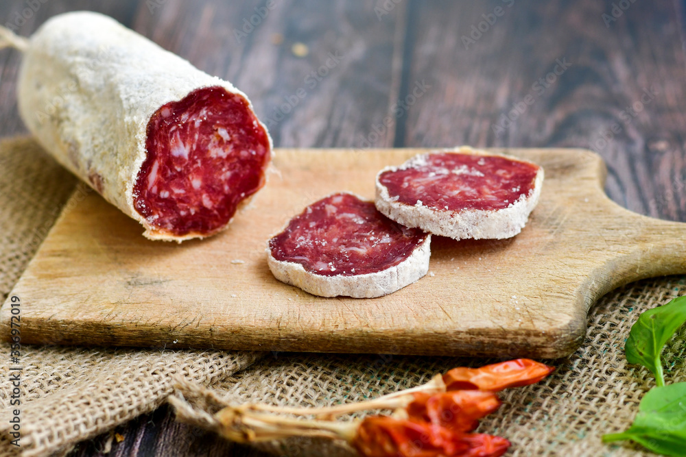 Italian  dried   artisan  pork salami,parmesan cheese ,peperoncino  and fresh basil on wooden background .Rustic  home made food