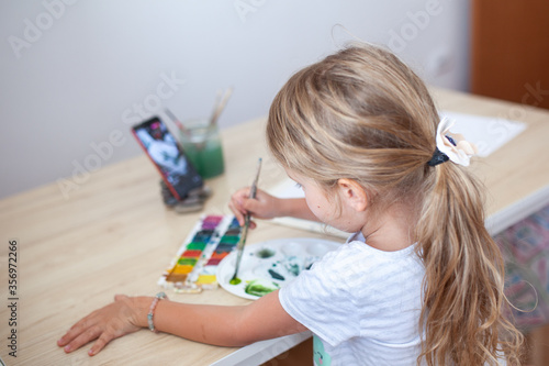 work from home with kids. Little child girl draws And watches a drawing lesson online on a tablet in home. Mom works on a computer at home. quarantin