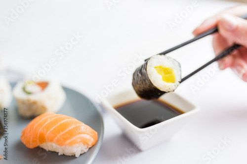 Close up of woman holding sushi roll with chopsticks above bowl with soy sauce at the table. Healthy meal concept.