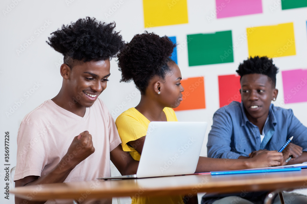 Obraz premium Cheering african american male student at computer with group of students