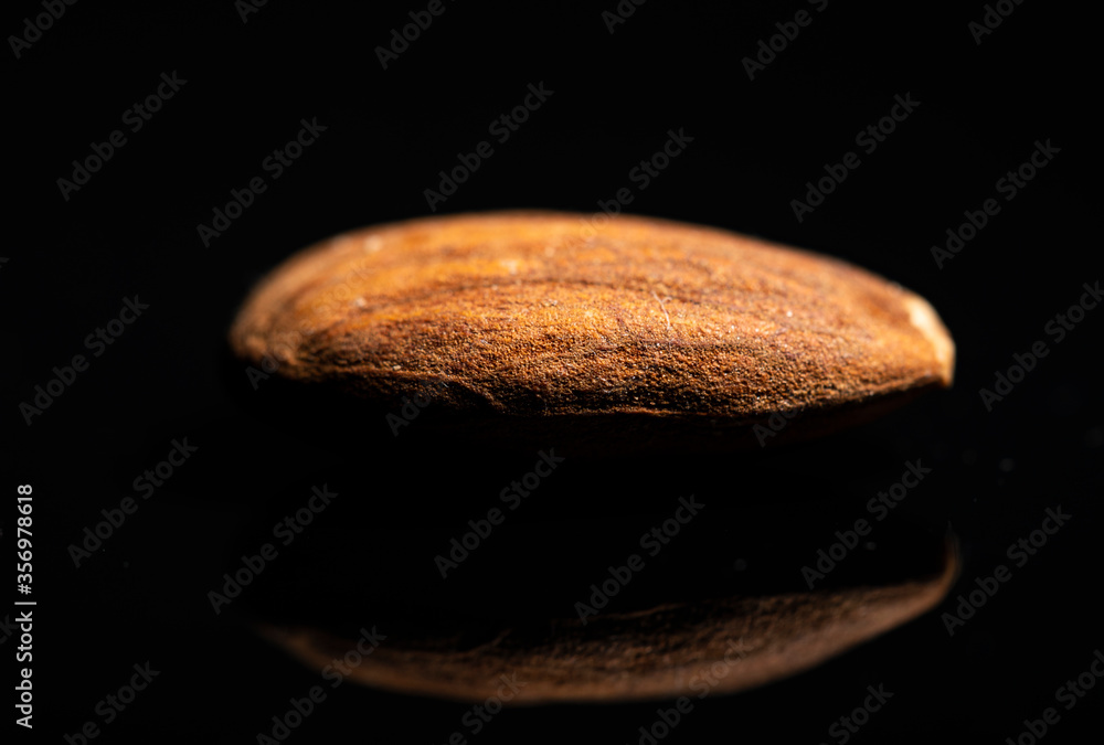 A close-up shot of a spot lit individual almond on a black reflective surface. A close-up shot of a spot lit individual almond on a black reflective surface.