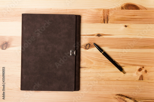 Leather-bound business notebook with a black pen on wooden background. Business concept