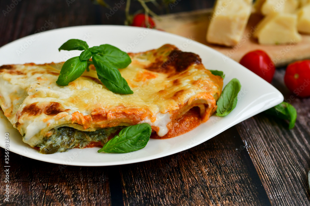 Delicious Home made Lasagna with minced meat,tomato sauce and spinach on a wooden rustic background.Home made italian meal Delicious Home made Lasagna with minced meat,tomato sauce and spinach on a wooden rustic background.Home made italian meal