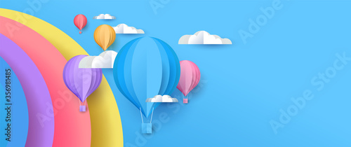 Cute papercut sky landscape background with copy space. Hot air balloon, rainbow and clouds made in realistic paper craft art or origami style for baby nursery, children design. 