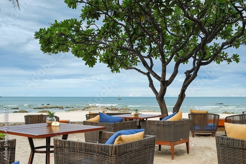 Photography View to Alfresco cafe with cozy rattan furniture and plumeria tree on ocean beach terrace