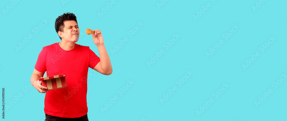 handsome Asian man is eating fried chicken deliciously on blue background in studio With copy space. handsome Asian man is eating fried chicken deliciously on blue background in studio With copy space.
