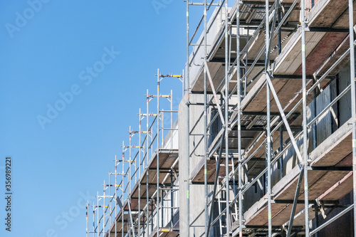 Konzept Baustelle: Die Fassade eines großen Gebäudes ist komplett eingerüstet für die Sanierung und viel blauer Himmel – sehr viel Copyspace, selektiver Fokus