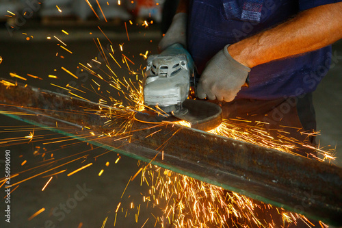 A man works in a factory with metal,sparks frying over the working table during metal grinding,craftsman sawing metal with disk grinder in workshop.