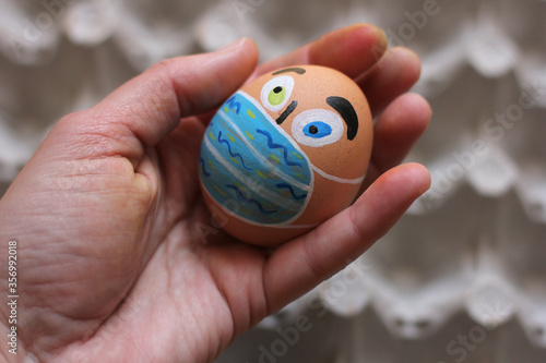 Wallpaper Mural Painted Easter egg like human face with protective masks in the human hand, eggs carton on the background Torontodigital.ca
