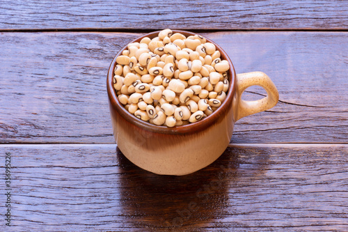 Many grains of brown raw beans in cup on wooden table. photo