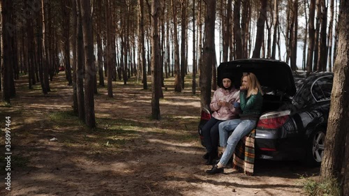 Two girlfriends on picnic in the woods near the trunk of the car