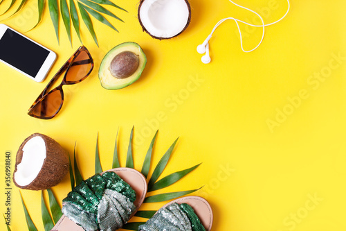Sunglasses, palm leaves, sandals and avocados on a yellow background. View from above