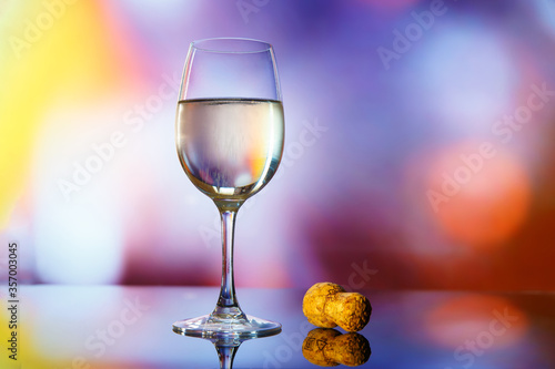 A glass of champagne and a cork from a bottle on a background of multi-colored lights.