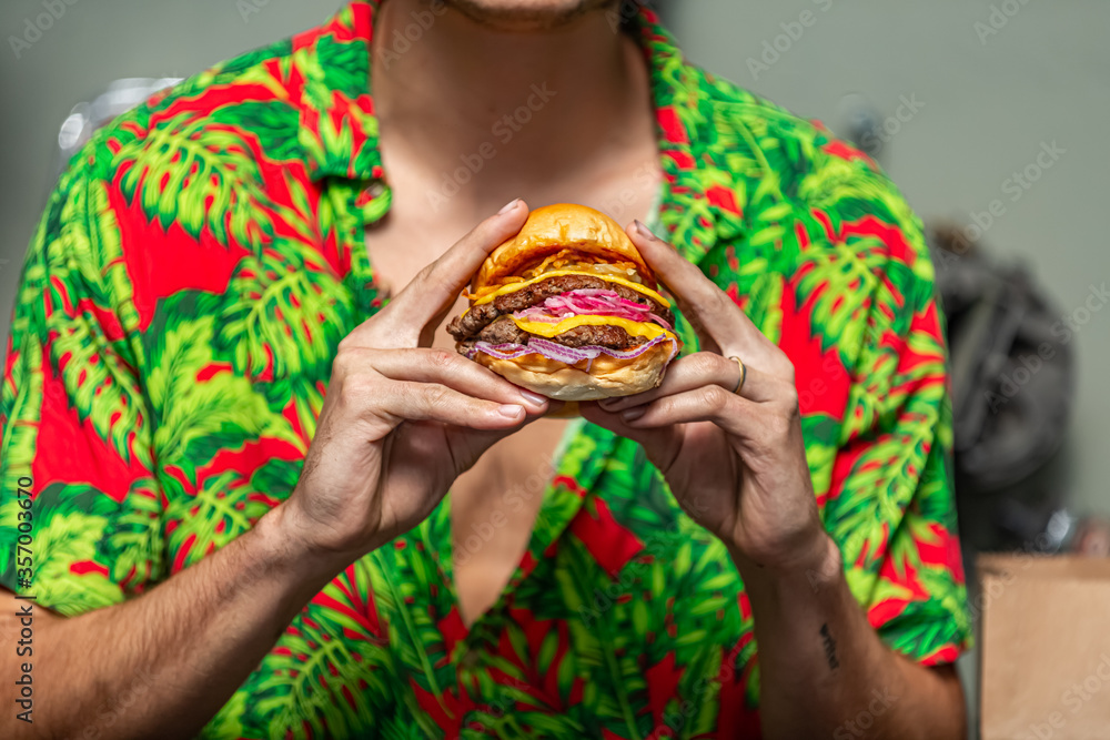 Young man holding a piece of hamburger. Eats fast food. Burger is not helpful food. Very hungry guy. Diet concept.