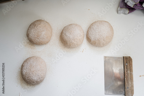 Top view of four raw sourdough bread buns dusted with spelt flour rising