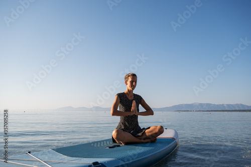 Young woman meditating on sup board floating on sea water