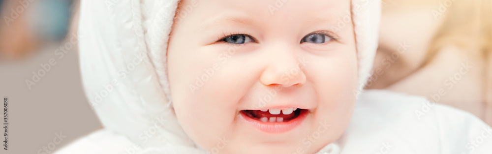 Cute smiling Caucasian baby girl outside. Child toddler in white warm clothes outdoor. Laughing funny lovely young kid face with blue eyes. Happy childhood lifestyle. Banner header for a website.