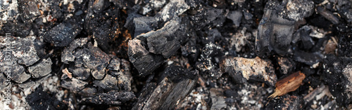 Natural ash charcoal fire place texture background. Closeup macro of burnt wood tree log. Dirty messy surface of firepit with copyspace. Banner header for a website.