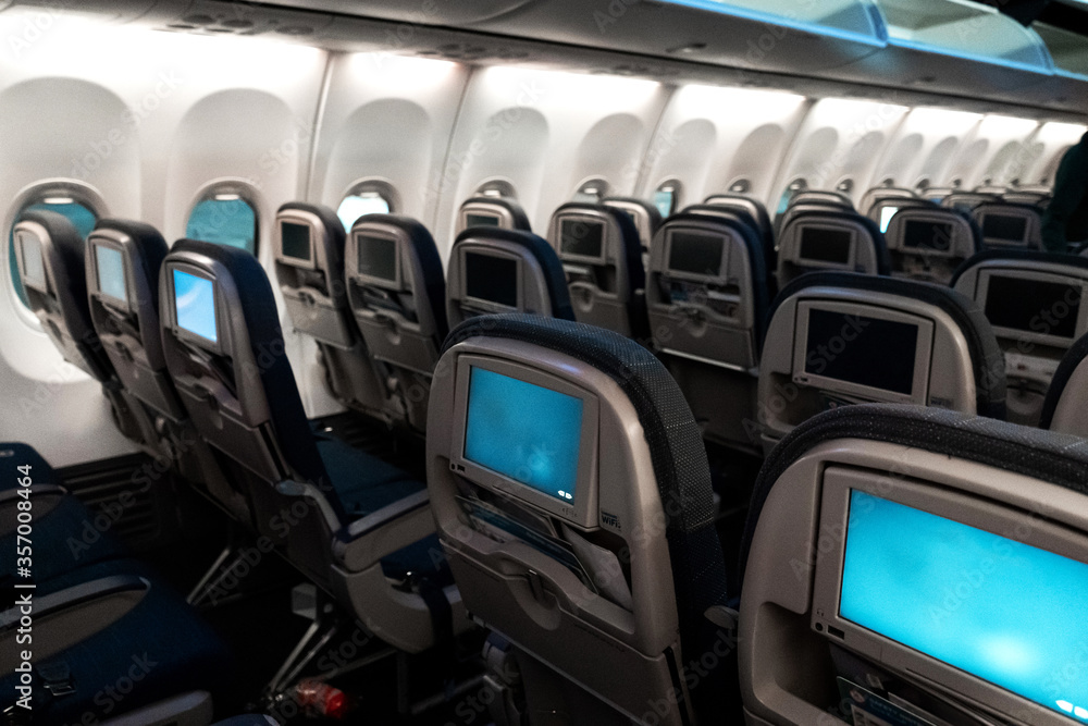Fototapeta premium The interior of the aircraft. Empty airplane cabin. Rows of passenger seats with screens in the head restraints