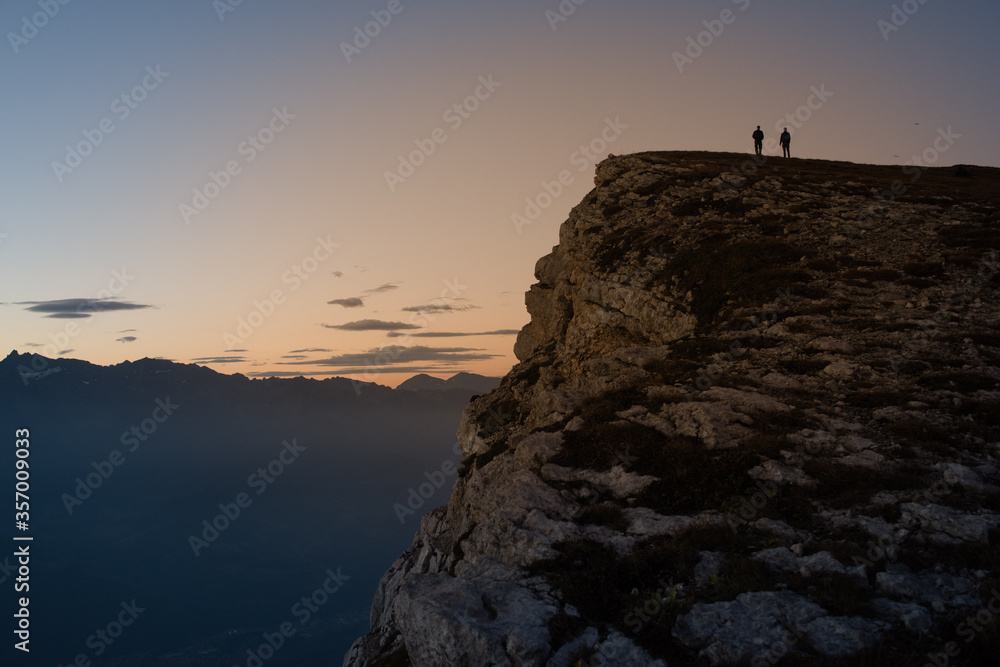 two people standing on a lonely mountain top at sunrise looking at the horizon.