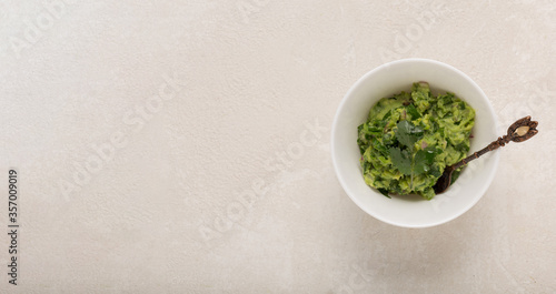 Mexican guacamole sauce in a white bowl on a concrete background, top , copy space