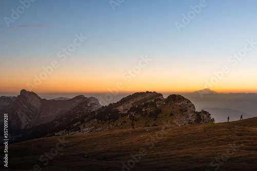 alpine landscape with mont blanc in the background at sunrise with two hikers and their tent .