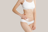 Slim young woman in underwear apply cream  to belly on beige background