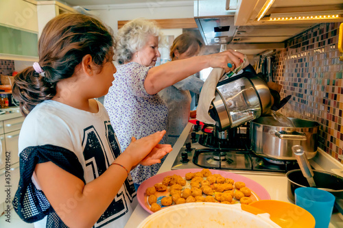 Three generation cooking: Turkish grandmother is teaching her grandchild traditional middle eastern cuisine. Girl preparing lentil balls. Elderly boiling water. Mother in kitchen background 