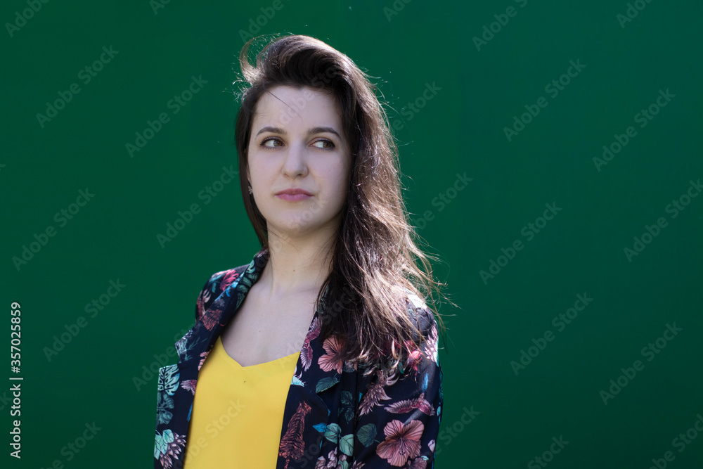 Attractive young brunette woman in yellow t-shirt and flowery shorts costume. green wall background. copy space. Attractive young brunette woman in yellow t-shirt and flowery shorts costume. green wall background. copy space.