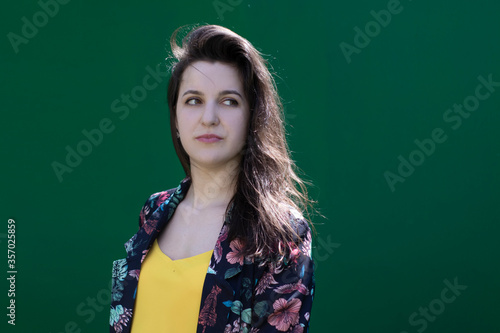 Attractive young brunette woman in yellow t-shirt and flowery shorts costume. green wall background. copy space. © OliaVesna