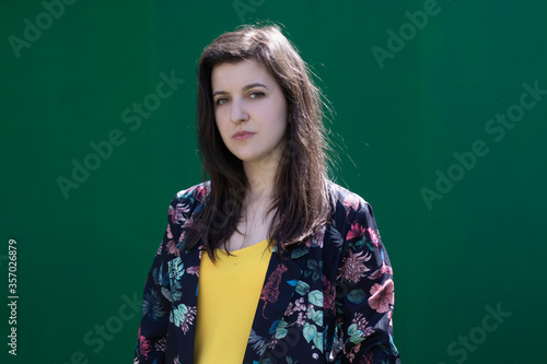 Attractive young brunette woman in yellow t-shirt and flowery shorts costume. green wall background. copy space. © OliaVesna