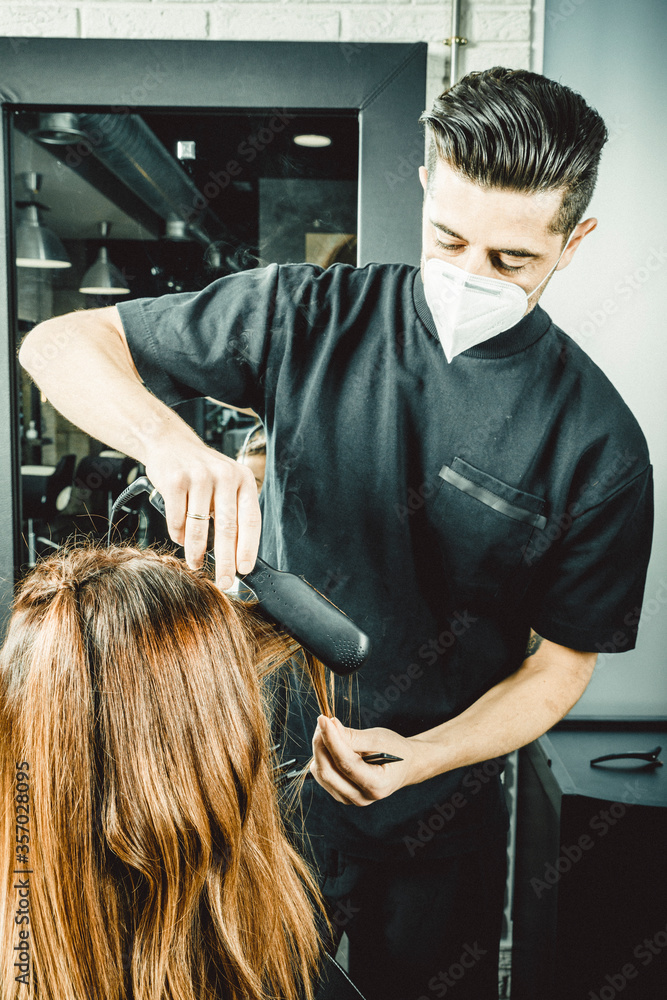 Naklejka premium Peluquero cortando el pelo a mujer con la mascarilla de protección puesta, por el virus COVID19