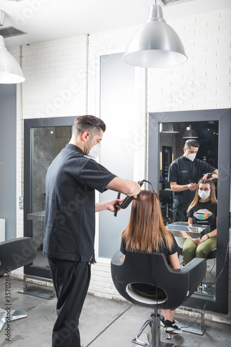 Peluquero cortando el pelo a mujer con la mascarilla de protección puesta, por el virus COVID19 photo