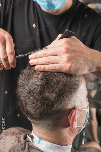 Peluquero cortando el pelo a cliente, ambos con la mascarilla de protección por el virus COVID19