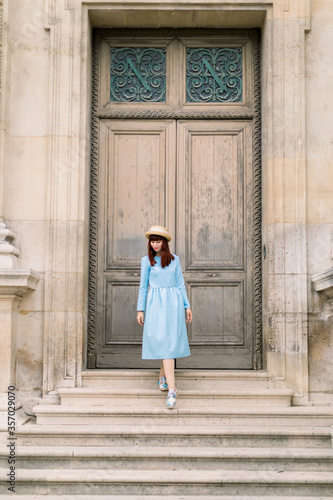 Photo of a beautiful young woman in blue dress descends the vintage stairs on the background of old building with doors © sofiko14