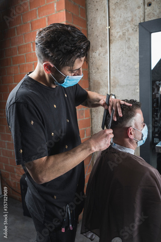 Peluquero cortando el pelo a cliente, ambos con la mascarilla de protección por el virus COVID19 photo