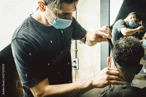 Peluquero cortando el pelo a cliente, ambos con la mascarilla de protección por el virus COVID19 photo