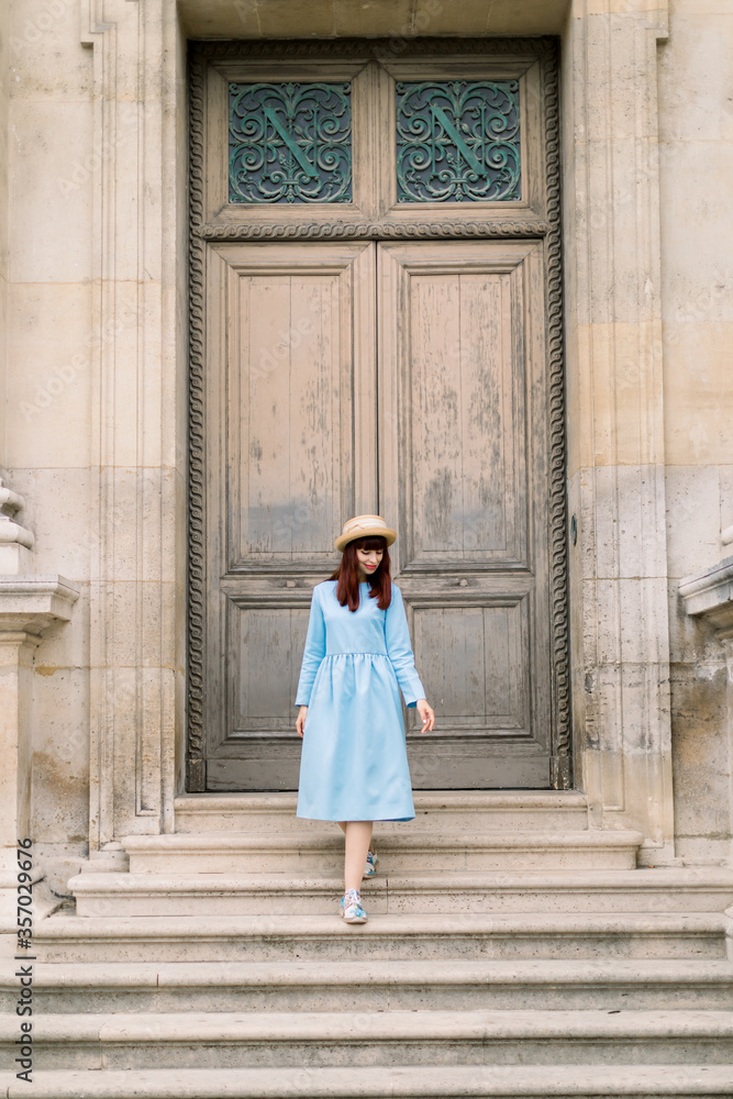 Photo of a beautiful young woman in blue dress descends the vintage stairs on the background of old building with doors