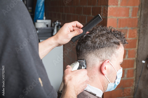 Peluquero cortando el pelo a cliente, ambos con la mascarilla de protección por el virus COVID19