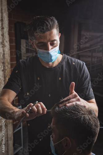 Peluquero cortando el pelo a cliente, ambos con la mascarilla de protección por el virus COVID19 photo