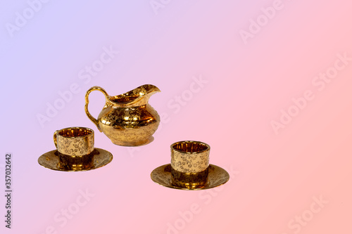 A beautiful gold plated pitcher and two espresso cups against a pastel background