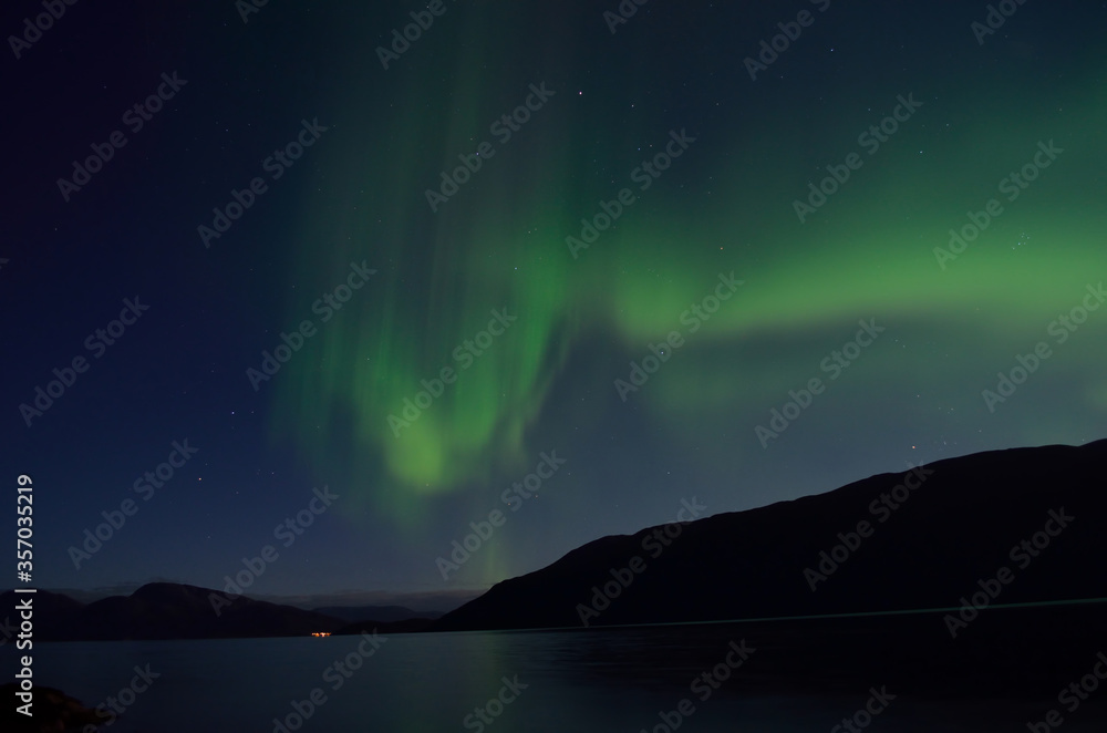 beautiful aurora borealis dancing over mountain and fjord landscape on late autumn night in northern Norway