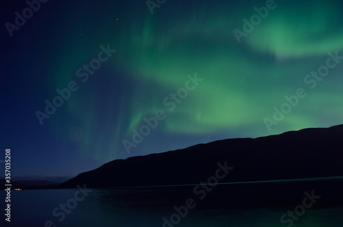 mighty aurora borealis dancing on night sky over mountain and fjord landscape in late autumn in the arctic circle